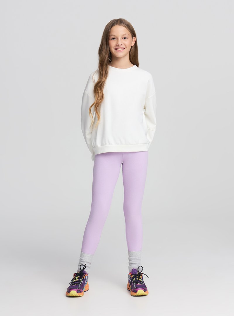 Felpa bianca con scollo rotondo, abbinata a leggings viola chiaro. Calzature con colori vivaci e suola testurizzata.
