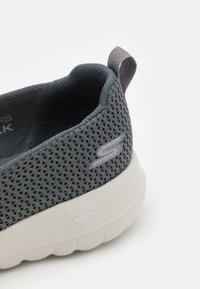 Baskets en mesh gris avec un dessus texturé et une semelle blanche épaisse. Comprend une doublure intérieure douce et une petite languette au talon.