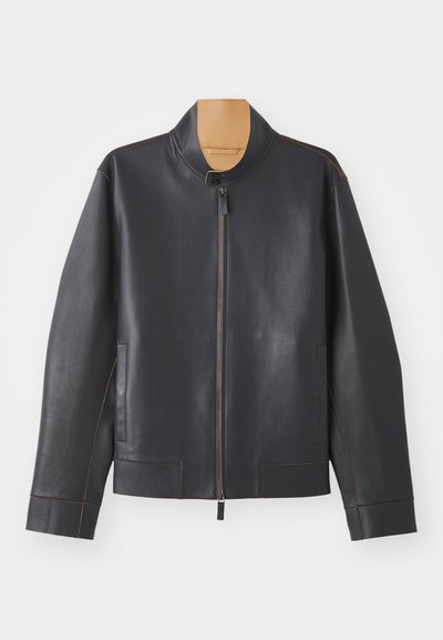 Schwarze Lederjacke mit Stehkragen, Reißverschluss und kontrastierendem braunem Näht. Sie verfügt über zwei Seitentaschen und ein schlankes Design.