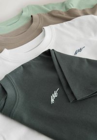 Neljä pyöreäkaulaista T-paitaa tummanvihreänä, valkoisena, vaaleanruskeana ja mintunvihreänä, joissa tummanvihreässä paidassa on pieni kirjailtu logo.