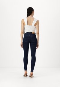 White, textured crop top with wide straps, paired with form-fitting, dark blue denim jeans featuring a mid-rise and back pockets.