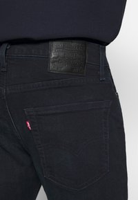 Mörkblå denimjeans med en läderlogotyp, bågformad sömnad på bakfickorna och en liten röd etikett nära vänsterfickan.