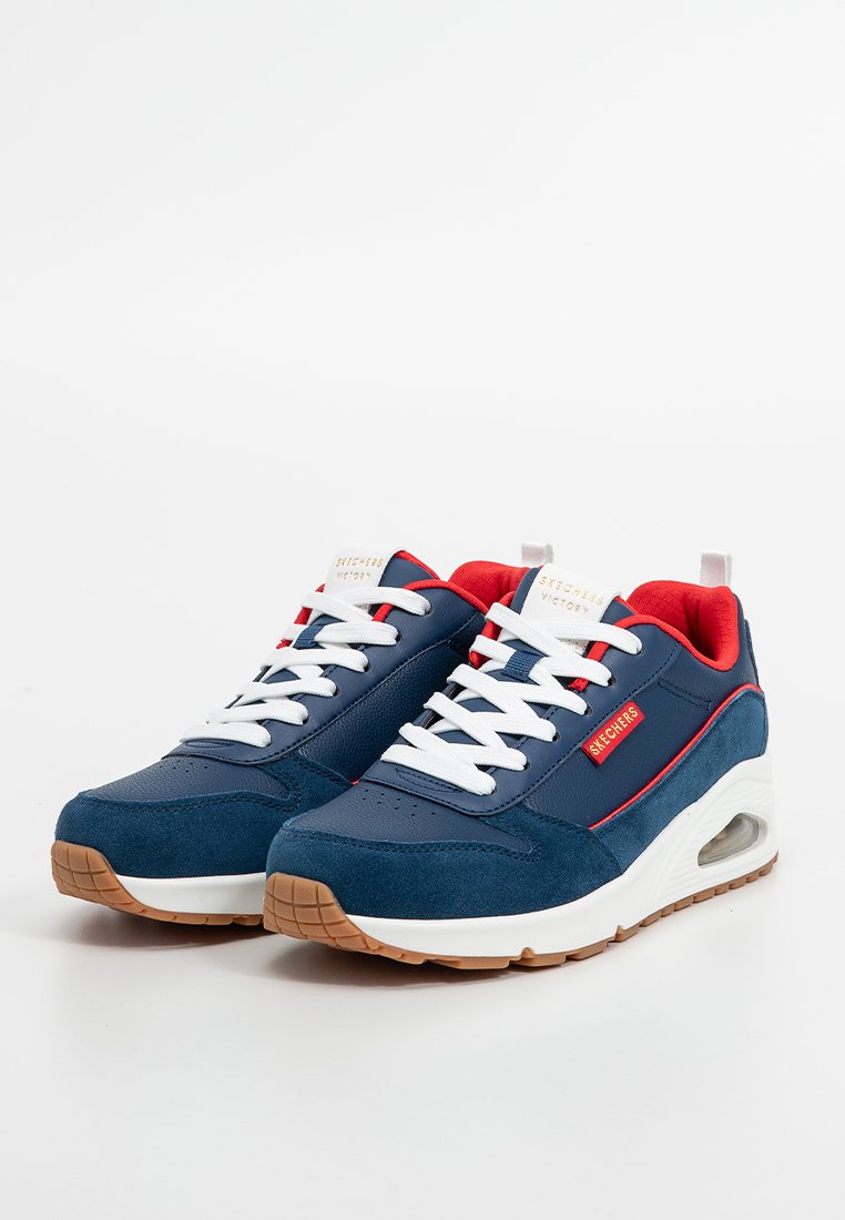 Baskets de sport bleu marine avec des accents rouges, en mesh et en suède, lacets blancs, semelle rembourrée et poche d'air visible sur le côté.