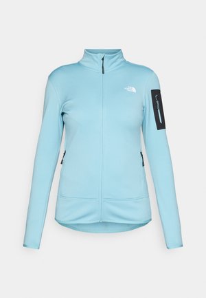 Lichtblauwe dames fleecejack met rits en hoge kraag, zwarte ritszak op de linkermouw, en het logo van The North Face op de borst.