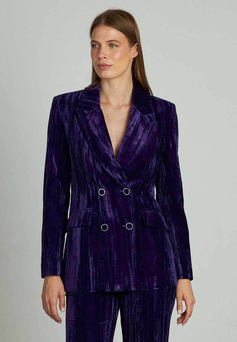 Blazer in velluto doppiopetto di un ricco viola con un leggero lucido, con rever affilati, due tasche frontali e dettagli in anello argentato.