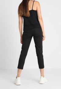 Débardeur noir à fines bretelles associé à un pantalon noir raccourci, porté avec des baskets blanches épaisses, mettant en valeur une tenue décontractée.