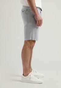 Shorts rayés gris clair en tissu respirant, dotés de poches latérales et d'une coupe confortable, associés à des baskets blanches.