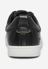 Baskets en cuir noir avec une texture lisse, dotées d'une semelle en caoutchouc blanche, de forme arrondie et d'une languette au talon pour un enfilage facile.