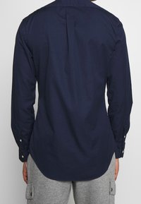 Mörkblå långärmad skjorta med knapp-ner krage och rundad nederkant. Tillverkad av slätt tyg med subtil textur och veck bak.