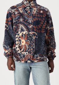 Pullover in pile con mezza cerniera in motivi floreali e geometrici blu, arancione e crema; vestibilità morbida con polsini ed orlo elastici.