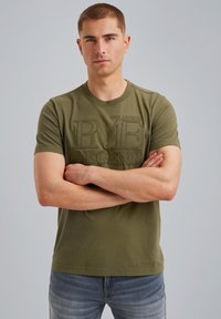 Olivgrön bomulls T-shirt med präglad text "PME LEGEND". Kort ärm och rund halsringning. Bärs med ljusblå jeans.
