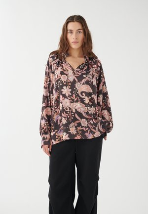 Blusa a maniche lunghe in tessuto scuro con motivi floreali e paisley rosa e viola, dotata di scollatura a V e vestibilità rilassata. Abbinata a pantaloni neri.