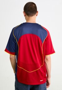 Rød og marineblå sports trøje med mesh-design, korte ærmer, rund halsudskæring og gule accenter langs sømmene og kanterne.