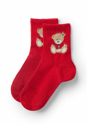 Rote Baumwollsocken mit einem plüschigen Teddybär-Design am Knöchel. Der Bär ist hellbraun mit schwarzem und weißem Akzent.