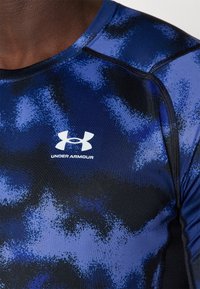 Blauw en zwart Under Armour aansluitend sportshirt met een getextureerd, abstract patroon en een contrasterend logo op de borst.