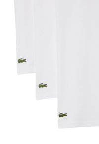 Tre T-shirt bianche in cotone a maniche corte, con logo di coccodrillo ricamato verde vicino all'orlo sul lato sinistro.
