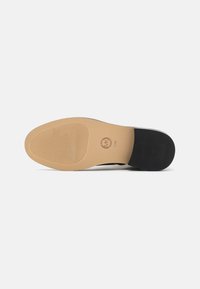 Black shoe outsole with a smooth texture, light tan rubber midsole, and ridged pattern for grip. Features a logo imprint.