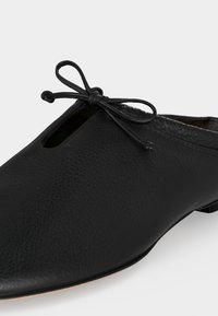 Μαύρο δερμάτινο παπούτσι χωρίς κορδόνια με μικρό φιόγκο μπροστά και ελαφρώς μυτερή μύτη.