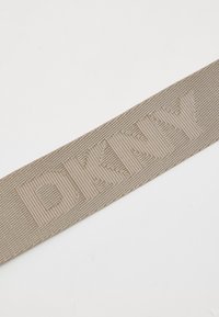 Cinturino in tessuto beige DKNY con logo intrecciato. Presenta una superficie testurizzata e un design piatto, evidenziando il nome del marchio in un carattere strutturato.