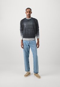 Pulover gradient negru și gri cu guler și mansete ribbrate, asortat cu blugi drepti de culoare albastru deschis și pantofi slip-on bej.