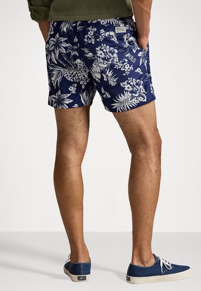 Shorts bleu marine avec un motif floral tropical blanc, poches latérales et une petite étiquette logo à l'arrière. Design de courte longueur.