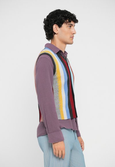 Canotta a maglia con righe multicolori e dettagli a treccia, indossata su una camicia viola. Presenta un design cropped e filato testurizzato.