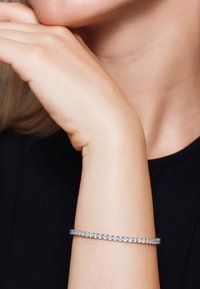 Bracciale d'argento con diverse pietre rotonde e scintillanti, incastonate in una sottile fascia, indossato su un polso contro una maglietta nera.