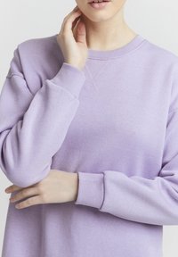 Violetti huppari, joka on valmistettu pehmeästä kankaasta, ja siinä on ribattu reunus. Ominaisuuksiin kuuluu pyöreä kaula-auko ja ristikkäisompelu etuosassa.