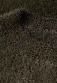 Tessuto verde scuro con una consistenza, caratterizzato da lunghe fibre morbide che creano un aspetto peloso. La superficie mostra un motivo naturale, leggermente irregolare.