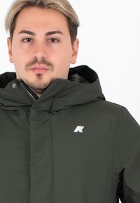 Giacca verde con cappuccio dal design elegante, realizzata in tessuto morbido. Presenta una chiusura con zip e un logo sul lato sinistro del petto.