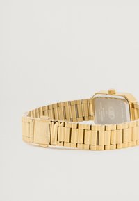 Gul rustfrit stålur med et rektangulært urværk, et tekstureret ledarmbånd og en lås med indgraveret branding på siden.