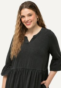 Černé bavlněné šaty s výstřihem do V, tříčtvrtečními rukávy a volánovými manžetami. Mají tiered design a přední kapsy. Měkká textura.