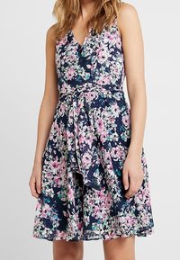 Blommig ärmlös klänning i marinblått med rosa och gröna blommor, V-ringning, åtsittande midja och ett knytband i tyg fram.