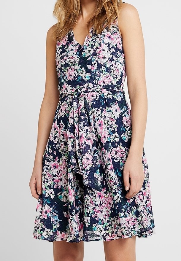 Blommig ärmlös klänning i marinblått med rosa och gröna blommor, V-ringning, åtsittande midja och ett knytband i tyg fram.