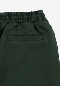 Ciemnozielone spodnie dresowe z elastycznym pasem, z małą kieszonką z tyłu i miękkim, teksturowanym materiałem.