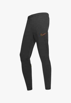 Pantaloni atletici neri a sigaretta con il logo Nike arancione sulla coscia e tasche laterali con cerniera, mostrati su sfondo bianco.