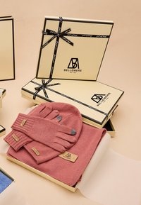 Rosa gestrickte Handschuhe und Mütze mit geripptem Muster, verpackt in einer beige Geschenkbox, geschmückt mit schwarzem Band und Markenetikett.