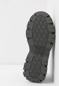 Šedá gumová podrážka obuvi se silnou, texturovanou vnější vrstvou s hlubokými drážkami a vyraženým logem. Velikost "37" viditelná na straně.