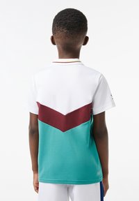 Koszulka polo z krótkim rękawem, z białą górą, wzorem w maroon i turkusowe chevron, o teksturowanej tkaninie i kontrastowym kołnierzyku.