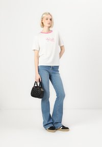 T-shirt branca de manga curta com decote rosa, apresentando gráficos de corações. Combinada com jeans azuis de cintura alta e uma pequena mala preta.