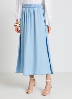 Donna che indossa una gonna midi azzurro chiaro con vita elasticizzata, sandali bianchi con tacco e top bianco a manica lunga con braccialetti d'oro.