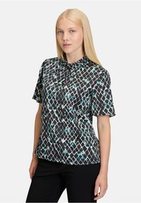 Korte mouwen blouse met een zwarte basis en een geometrisch patroon in turquoise en wit, met een kraag en een ontspannen fit. Zachte stoftextuur.