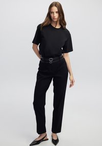 Černé tričko s krátkým rukávem v kombinaci s vysokými černými elegantními kalhotami, které mají pás s dvojitým sponou a špičaté černé baleríny.