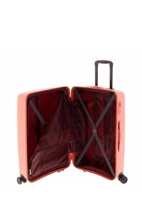 Valigia rigida rosa con scomparti chiusi da zip, fodera color amaranto e cinghie incrociate per fissare gli oggetti. Dotata di manico retrattile e ruote.