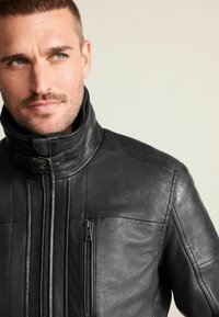 Zwarte leren jas met een hoge kraag, ritsluiting, voor- en zijritszakken, en gestructureerde panelen op de schouders en mouwen.