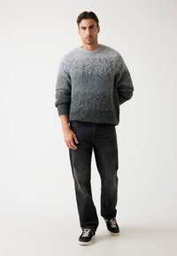 Maglione a maglia grigio sfumato con scollatura rotonda e maniche lunghe, abbinato a jeans scuri e sneakers. Tessuto morbido, vestibilità rilassata.