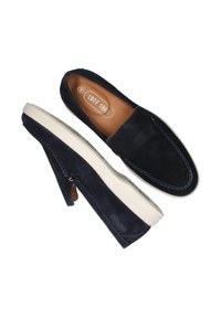 Chaussures en suede bleu marine à enfiler avec semelles en caoutchouc blanches, présentant des détails en couture et une semelle en cuir étiquetée "LOFF 1881."