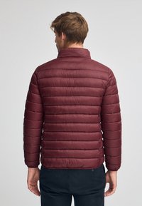 Bordeaux, puffjacka med hög krage, med horisontell sömnad, lättviktig tyg och en figursydd design. Visad bakifrån.