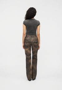 Γκρι ε φαρμοστό πουκάμισο με κοντά μανίκια, συνδυασμένο με ψηλόμεσα flare τζιν με φθαρμένη καφέ υφή και πίσω τσέπες.