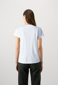 Hvid bomulds t-shirt med korte ærmer og lige pasform, parret med sorte jeans. Enkel bagudskuende, minimalistisk design, ingen synlige mønstre.